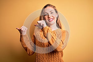 Young beautiful blonde woman wearing casual sweater standing over yellow background Pointing to the back behind with hand and