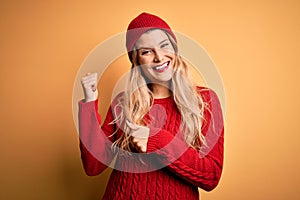 Young beautiful blonde woman wearing casual sweater and wool cap over white background Pointing to the back behind with hand and