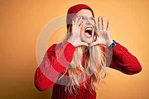 Young beautiful blonde woman wearing casual sweater and wool cap over white background Shouting angry out loud with hands over