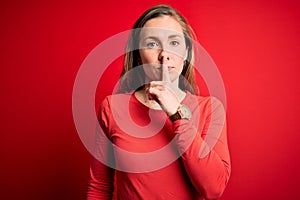 Young beautiful blonde woman wearing casual t-shirt standing over isolated red background asking to be quiet with finger on lips