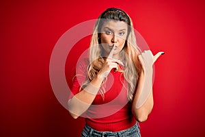 Young beautiful blonde woman wearing casual t-shirt standing over isolated red background asking to be quiet with finger on lips