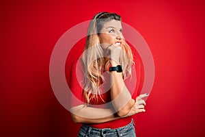 Young beautiful blonde woman wearing casual t-shirt standing over isolated red background Thinking worried about a question,