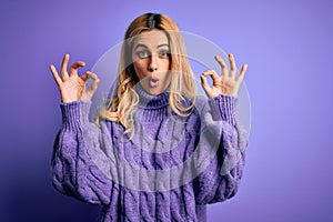 Young beautiful blonde woman wearing casual turtleneck sweater over purple background looking surprised and shocked doing ok