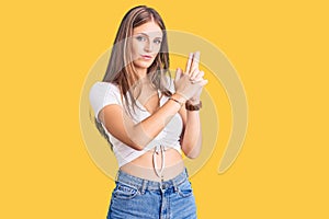 Young beautiful blonde woman wearing casual white tshirt holding symbolic gun with hand gesture, playing killing shooting weapons,