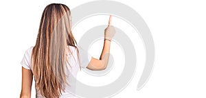 Young beautiful blonde woman wearing casual white tshirt posing backwards pointing ahead with finger hand