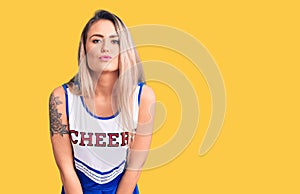 Young beautiful blonde woman wearing cheerleader uniform looking at the camera blowing a kiss on air being lovely and sexy