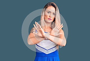 Young beautiful blonde woman wearing cheerleader uniform rejection expression crossing arms doing negative sign, angry face