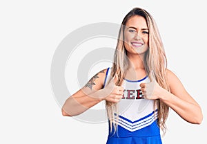 Young beautiful blonde woman wearing cheerleader uniform success sign doing positive gesture with hand, thumbs up smiling and