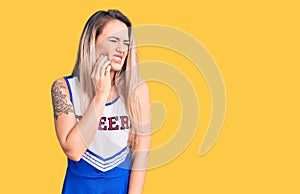 Young beautiful blonde woman wearing cheerleader uniform touching mouth with hand with painful expression because of toothache or