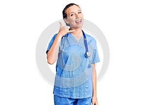 Young beautiful blonde woman wearing doctor uniform and stethoscope smiling doing phone gesture with hand and fingers like talking