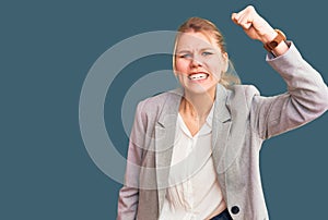 Young beautiful blonde woman wearing elegant jacket angry and mad raising fist frustrated and furious while shouting with anger