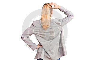Young beautiful blonde woman wearing elegant jacket backwards thinking about doubt with hand on head