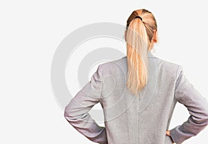 Young beautiful blonde woman wearing elegant jacket standing backwards looking away with arms on body