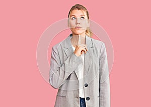 Young beautiful blonde woman wearing elegant jacket thinking concentrated about doubt with finger on chin and looking up wondering