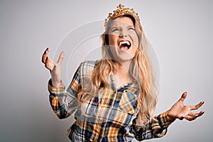 Young beautiful blonde woman wearing golden crown of queen over isolated white background crazy and mad shouting and yelling with