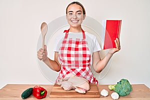 Young beautiful blonde woman wearing professional baker apron reading cooking recipe book smiling with a happy and cool smile on