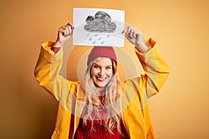 Young beautiful blonde woman wearing raincoat and wool cap holding banner with cloud image with a happy face standing and smiling