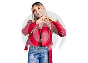 Young beautiful blonde woman wearing red leather jacket smiling in love showing heart symbol and shape with hands