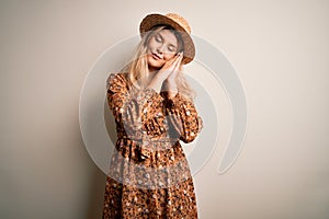Young beautiful blonde woman wearing summer dress and hat over isolated white background sleeping tired dreaming and posing with
