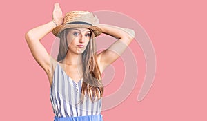 Young beautiful blonde woman wearing summer hat doing bunny ears gesture with hands palms looking cynical and skeptical