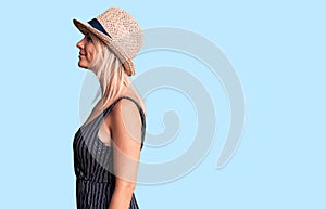 Young beautiful blonde woman wearing summer hat and dress looking to side, relax profile pose with natural face with confident