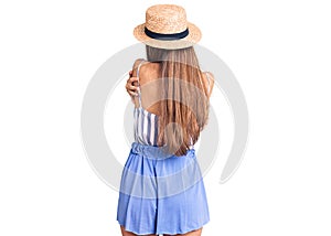 Young beautiful blonde woman wearing summer hat hugging oneself happy and positive from backwards