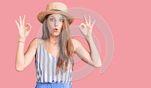 Young beautiful blonde woman wearing summer hat looking surprised and shocked doing ok approval symbol with fingers