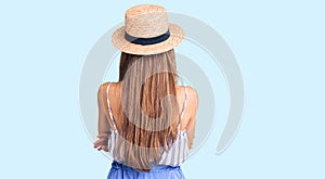 Young beautiful blonde woman wearing summer hat standing backwards looking away with crossed arms