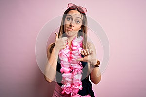 Young beautiful blonde woman wearing swimsuit and floral Hawaiian lei over pink background Doing thumbs up and down, disagreement