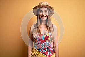 Young beautiful blonde woman wearing swimsuit and summer hat over yellow background with a happy and cool smile on face