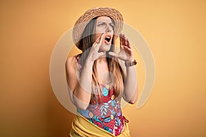 Young beautiful blonde woman wearing swimsuit and summer hat over yellow background Shouting angry out loud with hands over mouth