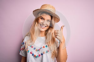 Young beautiful blonde woman wearing t-shirt and hat over isolated pink background doing happy thumbs up gesture with hand