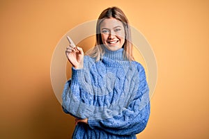 Young beautiful blonde woman wearing turtleneck sweater over yellow isolated background with a big smile on face, pointing with