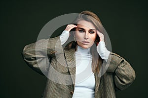 A young beautiful blonde woman in a white turtleneck and a man`s jacket poses on a green olive background in the studio.