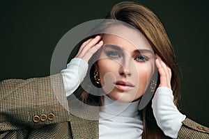 A young beautiful blonde woman in a white turtleneck and a man`s jacket poses on a green olive background in the studio.