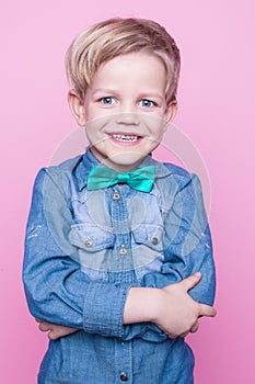 Young beautiful boy with blue shirt and butterfly tie. Studio portrait over pink background.