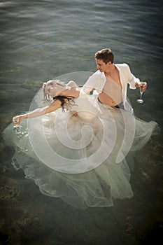 Young beautiful bridal couple dancing in rock pool with glasses