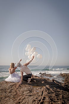 Young beautiful bridal couple having fun with white balloons at the beach