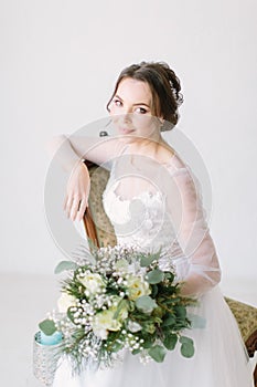 Young beautiful bride sitting in a chair and smiling, close-up. Beauty portrait of bride wearing fashion wedding dress