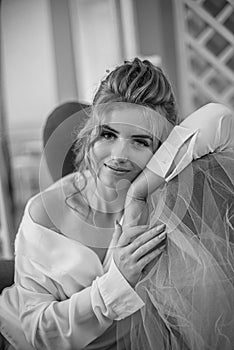 Young beautiful bride with wedding hairdo and makeup in the morning wearing a white silk negligee in the bedroom