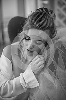 Young beautiful bride with wedding hairdo and makeup in the morning wearing a white silk negligee in the bedroom