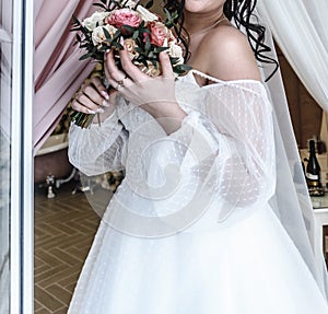 young beautiful bride in a white delicate elegant airy wedding dress with a bouquet of flowers rose