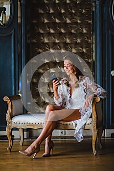 Young beautiful bride in white negligee watching a message in her smartphone