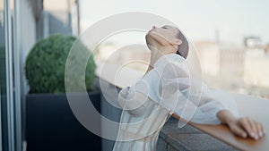 Young beautiful bride in a white wedding dress standing on a balcony on blurred city background. Action. Elegant woman