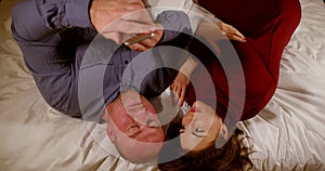 A young beautiful brown-haired girl in a red dress lies on a crumpled white bed next to a bald middle-aged man, moves