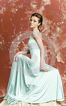 Young beautiful brown-haired woman in blue light silk dress with open shoulders and a long skirt and sandals