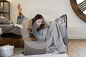 Young beautiful bruenette woman in cozy sweater in bed at home working on a laptop