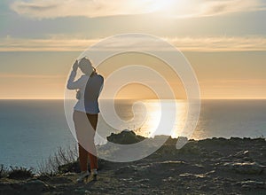 Young beautiful brunete woman in a white jacket and red pants, standing on a cliff over the sea and wait for a call. back view.