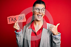 Young beautiful brunette businesswoman holding papaer with tax day message pointing and showing with thumb up to the side with