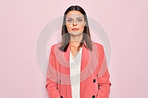 Young beautiful brunette businesswoman wearing elegant jacket over  pink background Relaxed with serious expression on